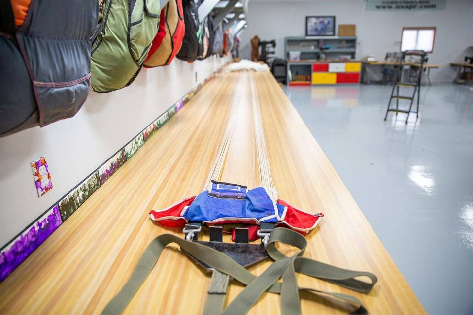 Red and blue parachute container with lines extended on a packing table at USAPR