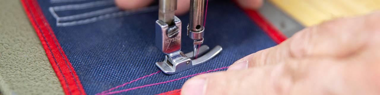 Two hands stitching a pattern on a blue patch of fabric