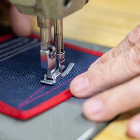Two hands stitching a pattern on a blue patch with a sewing machine